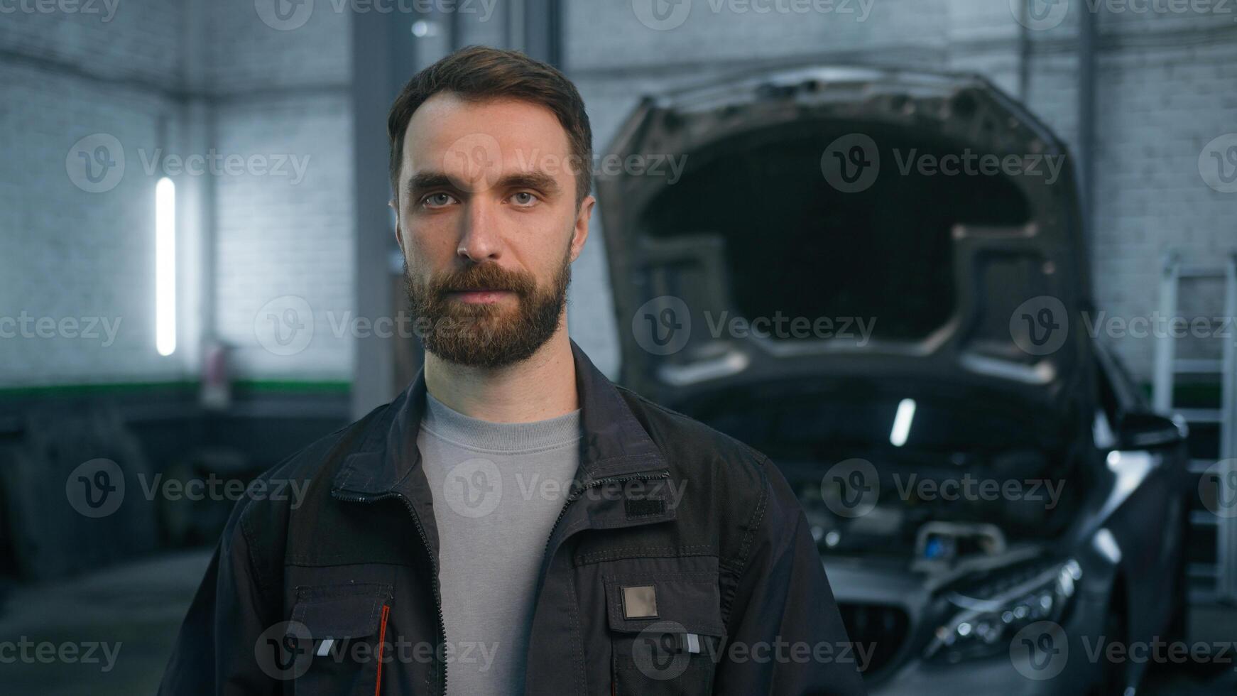 Professional auto mechanic adult bearded 30s man Caucasian male guy serious looking at camera in workshop automobile motorcar truck repair service center posing on electric car open bonnet background photo