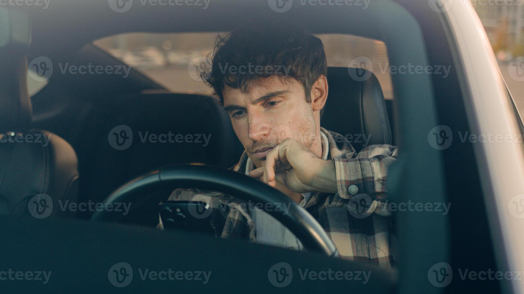 Displeased upset sad Caucasian man guy male driver car owner inside automobile on parking lot using mobile phone problem with smartphone read bad news frustrated anxious millennial driving auto city photo