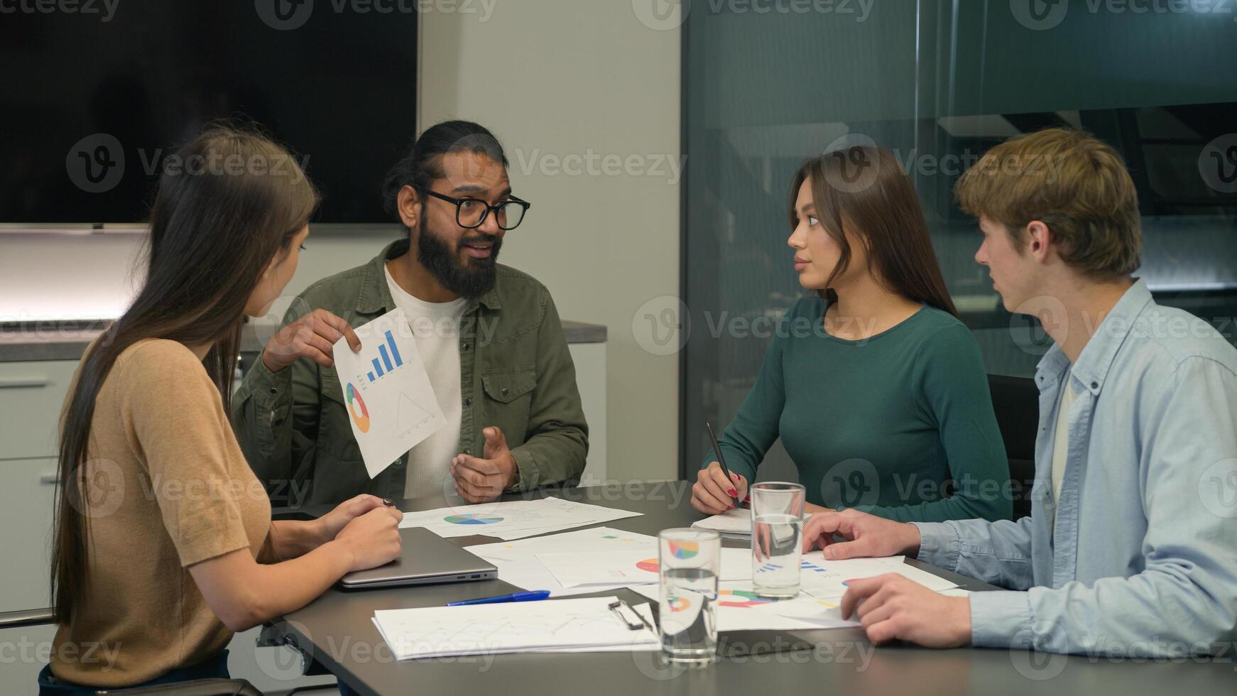 Office conference meeting male chief coach businessman talking to multiracial business team showing corporate sales charts graphs discuss strategy diverse women men colleagues employees listen leader photo