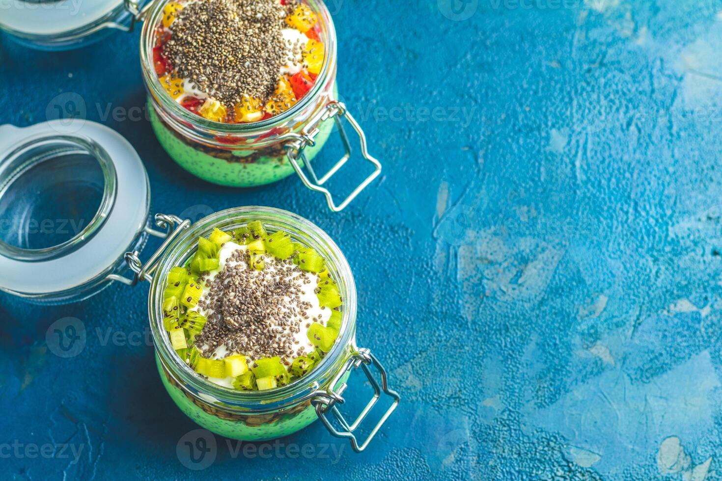 Layered chia seed pudding with kiwi and mango topping in glass jars on blue background photo