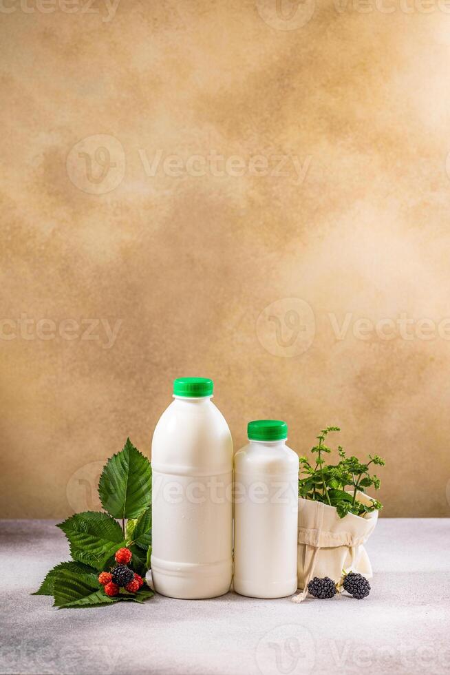 Two white bottles of milk or yogurt with green caps, berries and mint leaves displayed on table photo