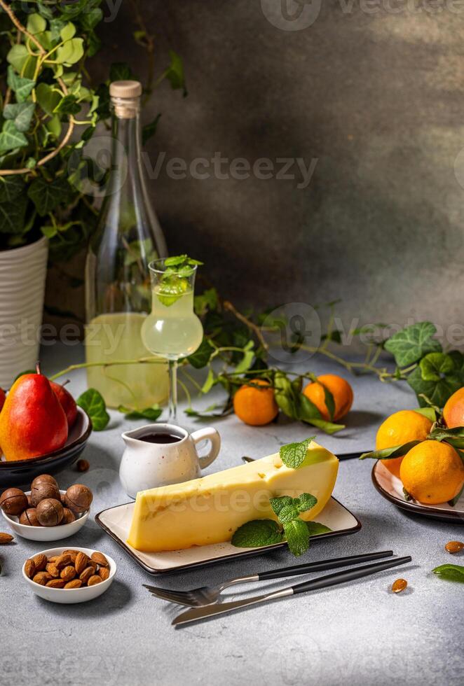 Gourmet cheese wedge with mint, fruits, nuts, and limoncello on table photo