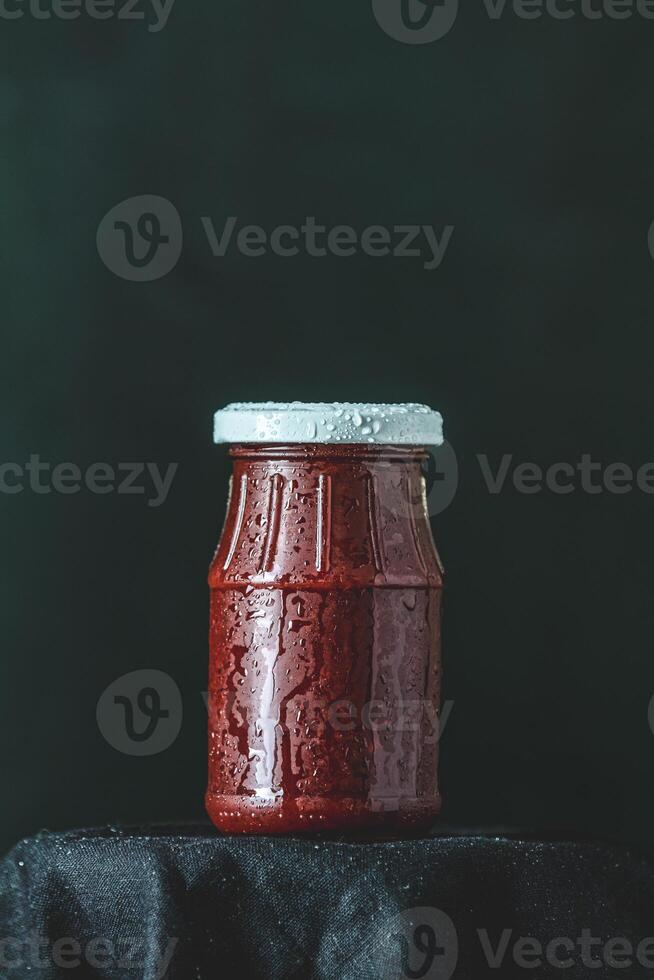 Small glass jar with red sauce resting on dark cloth photo