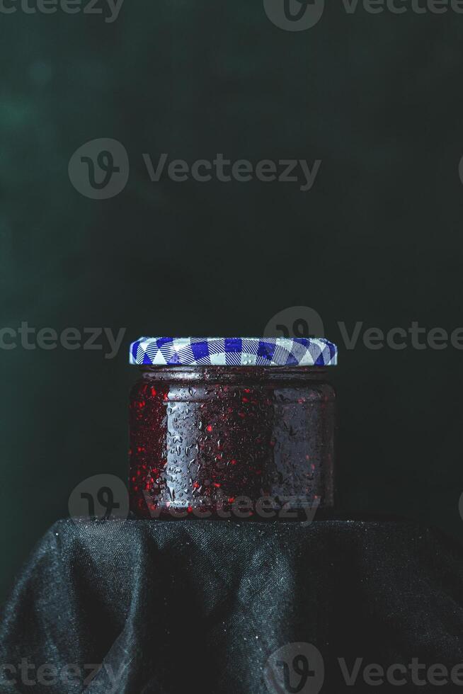 Jar of raspberry jam with checkered lid on black cloth photo