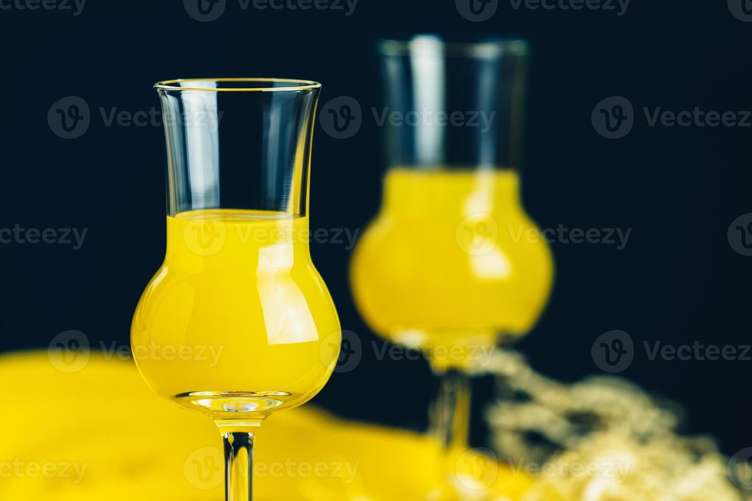 Two stemmed glasses with yellow liquor on a dark background photo