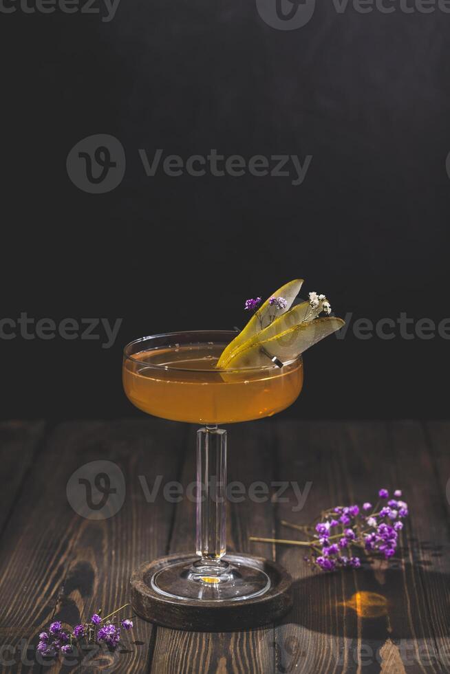 Elegant cocktail glass with pear slices and flowers on wooden table photo
