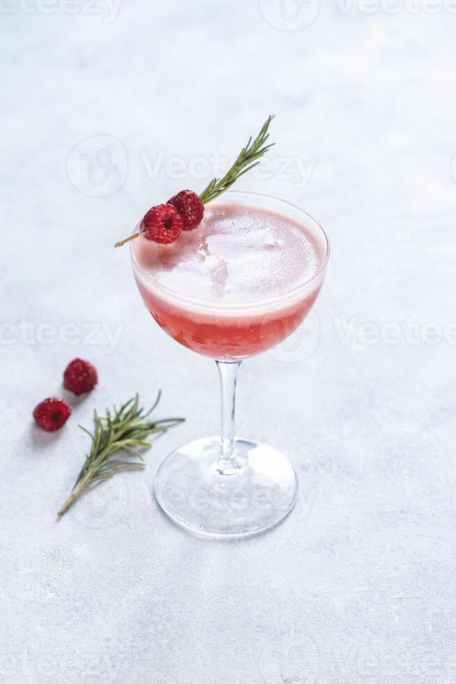 Refreshing pink raspberry cocktail garnished with rosemary in elegant glass photo