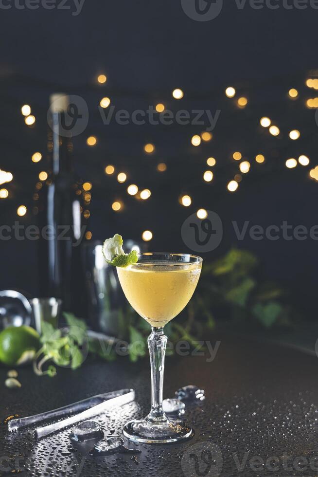Yellow cocktail garnished with lime and mint on wet countertop with bokeh background photo