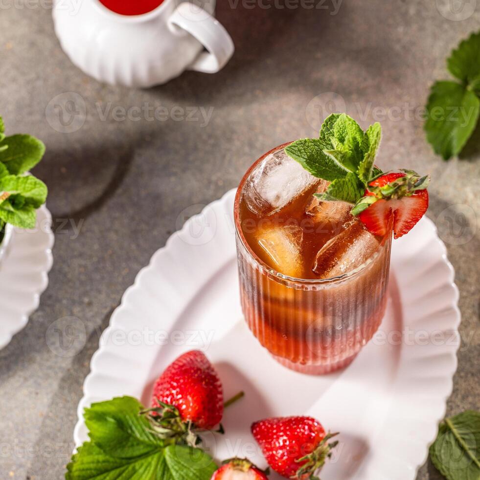 Glass of strawberry iced tea with ice cubes, fresh mint, strawberries, and a bowl of mint on a pink background, creating a refreshing summer drink photo