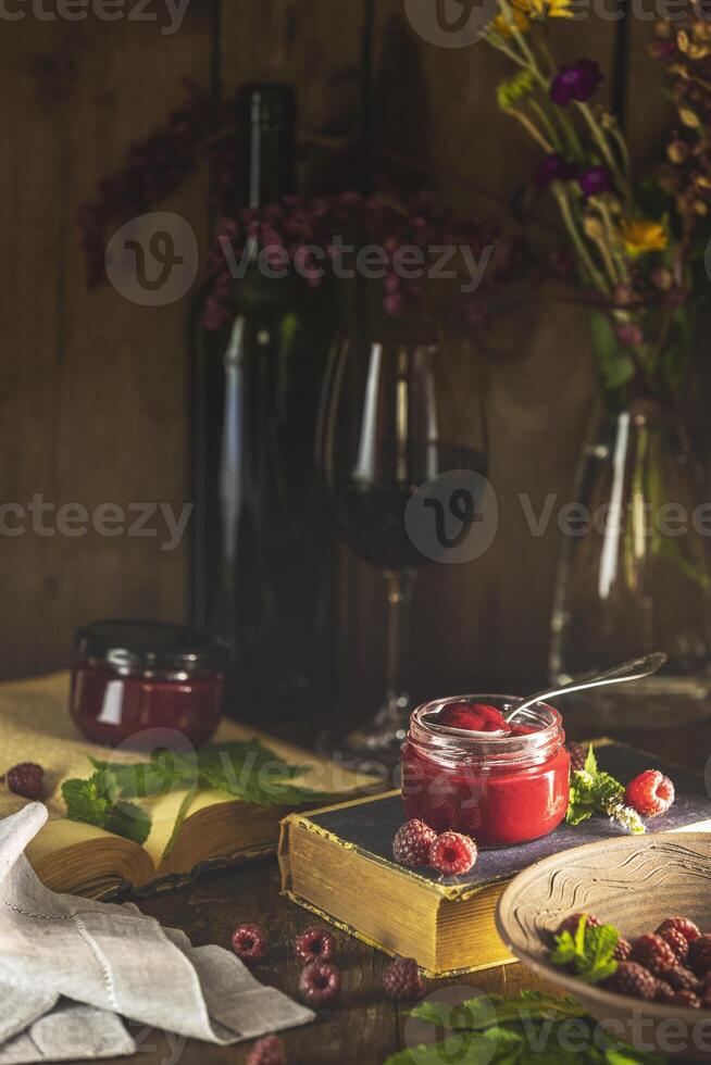 Raspberry jam with wine and old books on wooden table photo
