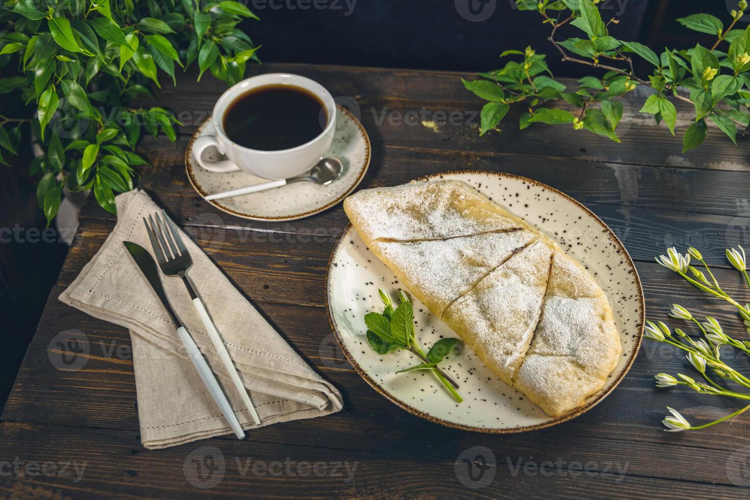 Apple strudel with powdered sugar served on a plate with a cup of coffee photo