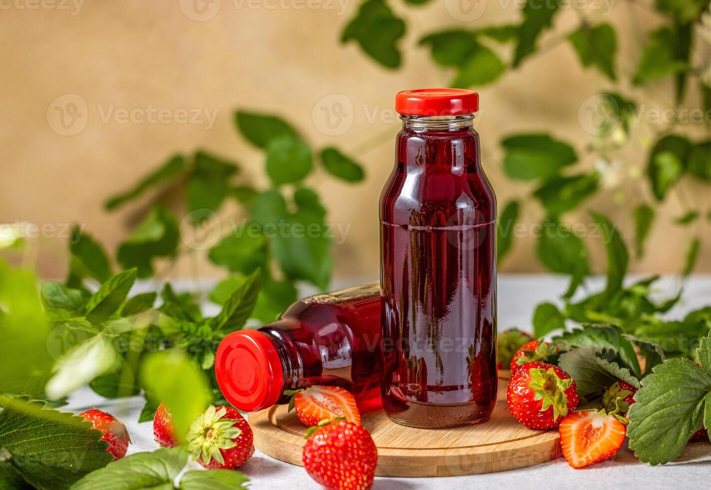Two bottles of fresh strawberry juice resting on wooden board with ripe strawberries and mint leaves photo