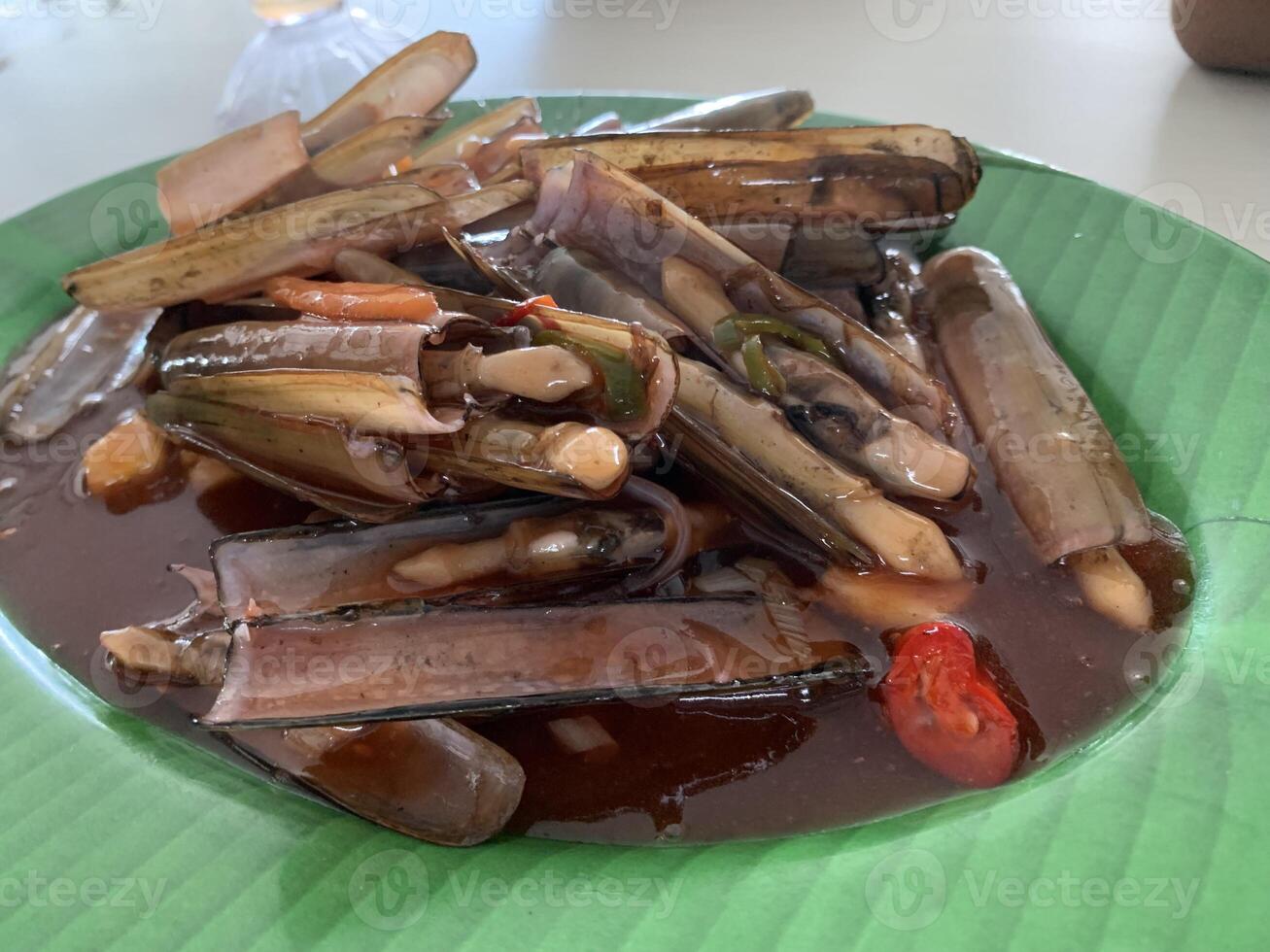 A Chinese Dish Bamboo clams steamed in sweet and sour sauce garnished with Spring Onions and Fried Garlic on green plate photo