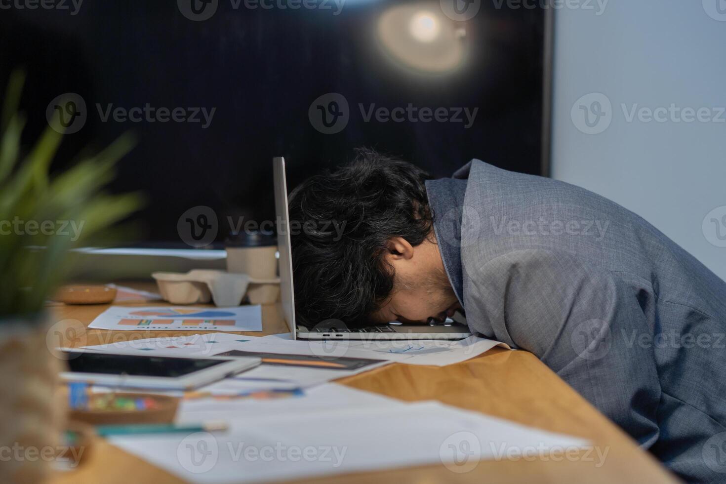 Side view of businessman heavy workload sleep on laptop at office desk with finance sheet calculator and coffee photo