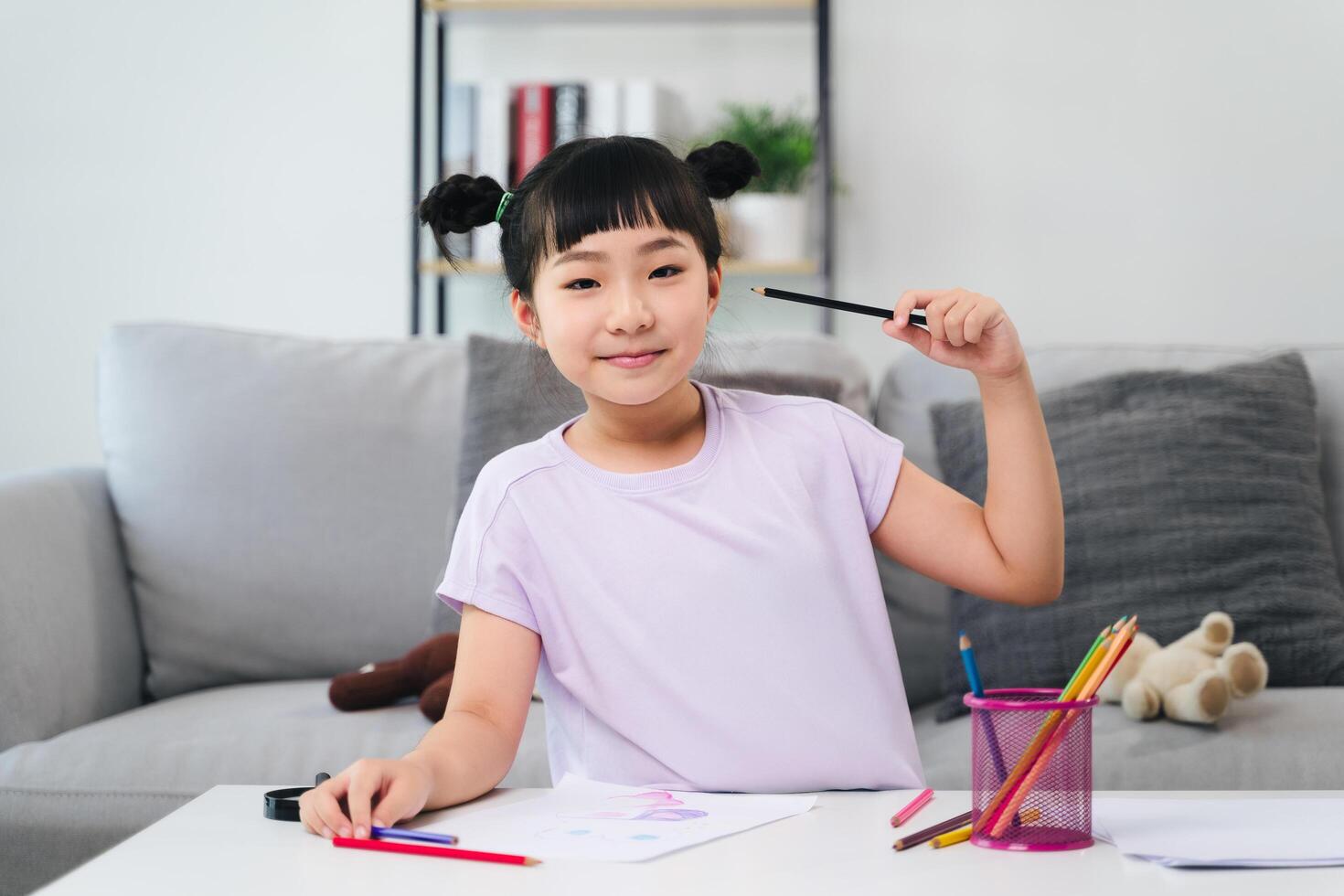 A cute young girl is engrossed in drawing and coloring with colored pencils on a blank piece of paper. photo