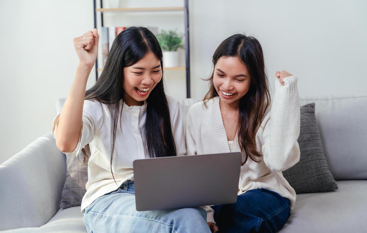 Two women are looking at a laptop screen and raising their arms in a gesture of joy and happiness photo