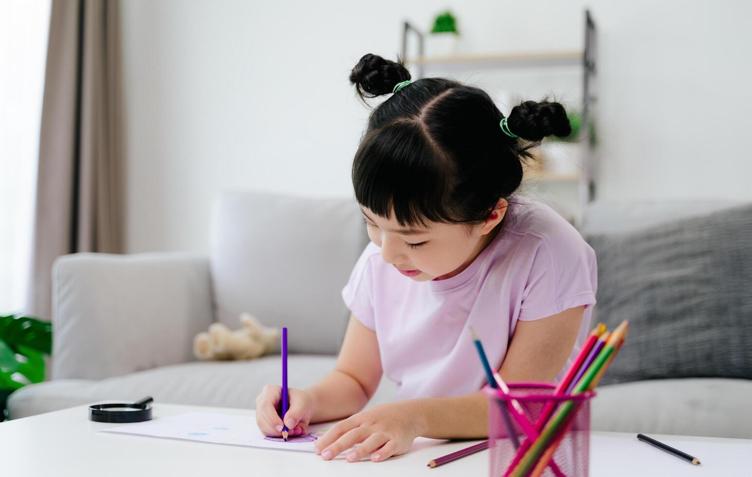 A cheerful young girl is sketching and filling her drawing with colored pencils on a sheet of paper. photo