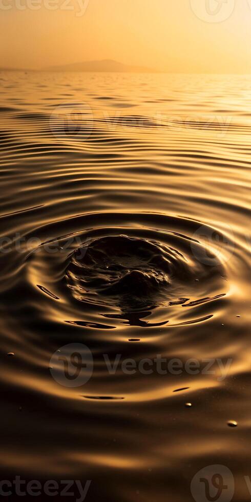 Rippling water surface reflecting golden hues, with a central disturbance creating circular waves photo