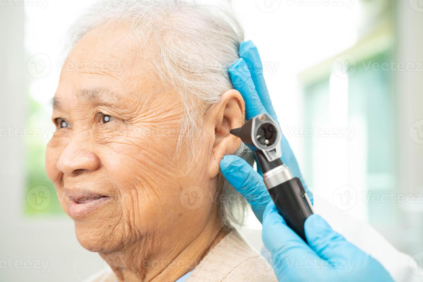 Otolaryngologist or ENT physician doctor examining senior patient ear with otoscope, hearing l photo