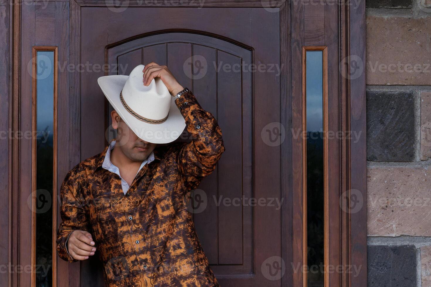 Mexican Cowboy adjusting his hat in front of a rustic wooden door photo