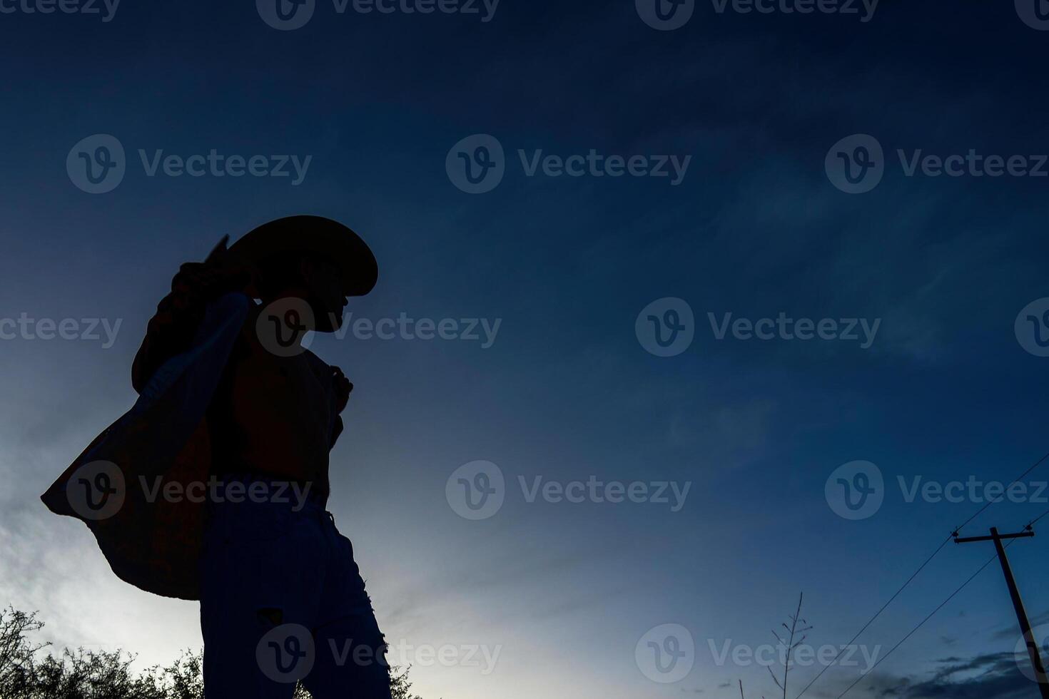 Mexican Cowboy Mexicano standing against the twilight sky with a hat in hand photo