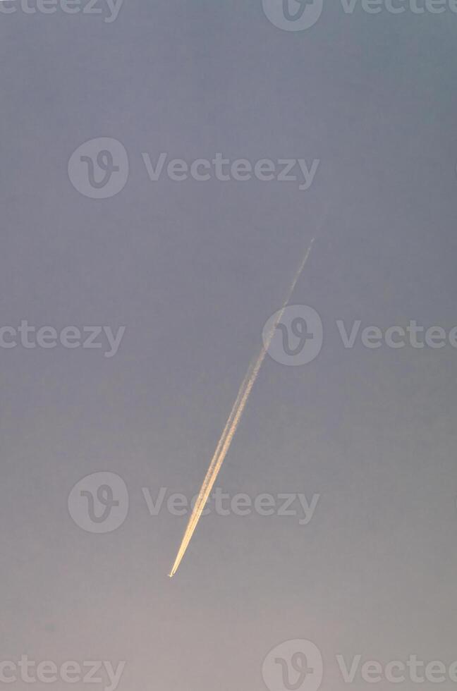 Airplane contrail streaking across a clear blue sky during twilight hours photo