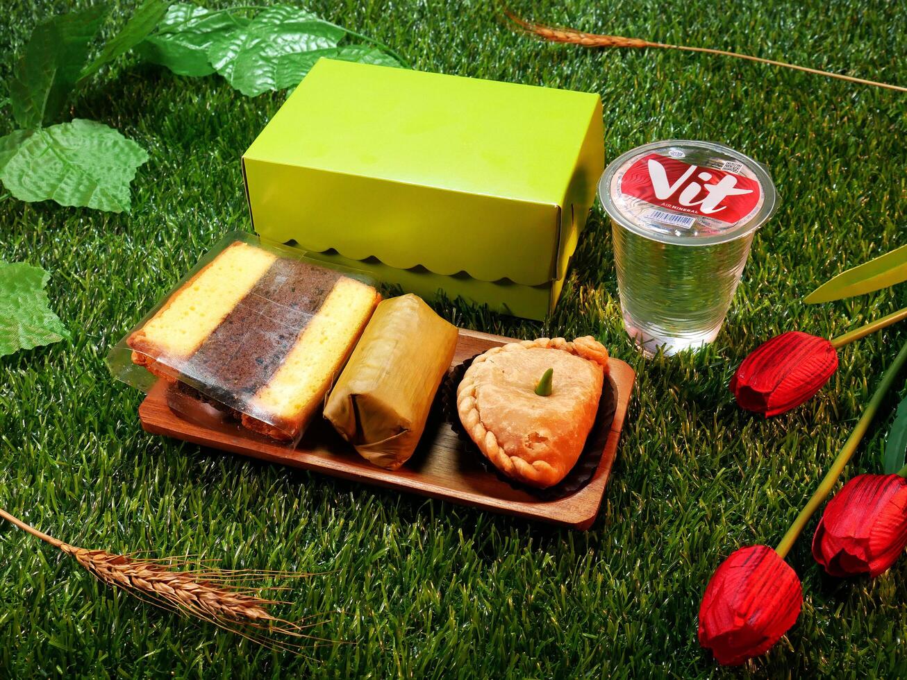 Jakarta, Indonesia. December 24, 2024. Snack box package traditional Indonesian cakes, layer cakes, lemper, and pastel or patty delicious and a glass of mineral water, with a natural decorative touch photo
