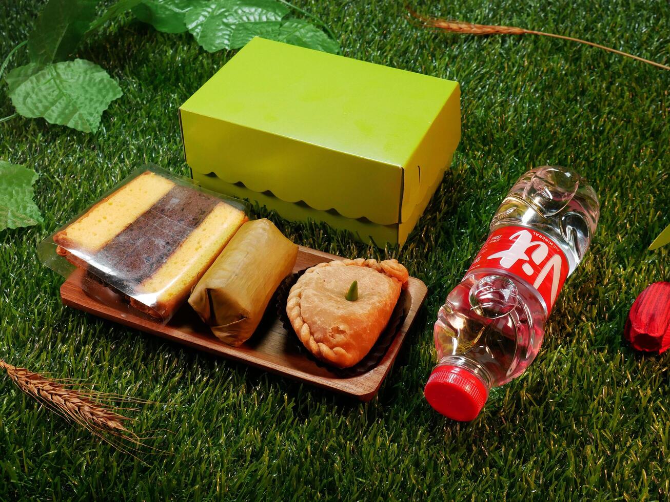 Jakarta, Indonesia. December 24, 2024. Snack box package traditional Indonesian cakes, layer cakes, lemper, and pastel or patty delicious and a bottle of mineral water, with a natural decorative touch photo