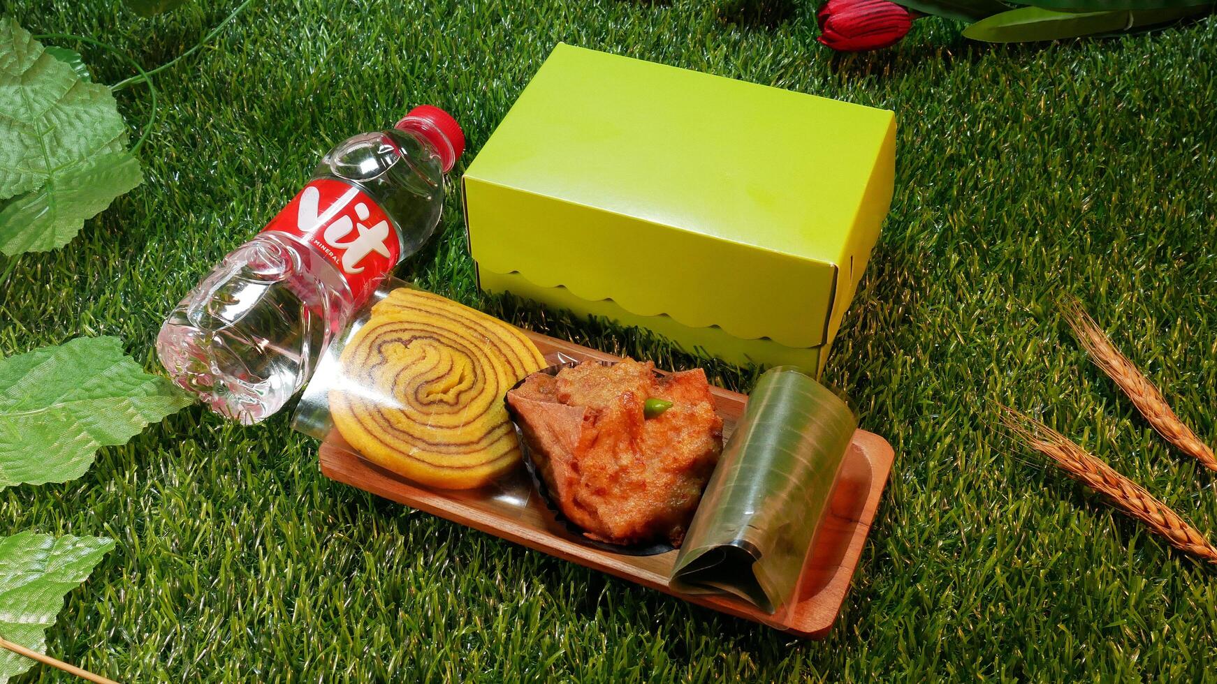 Jakarta, Indonesia. December 24, 2024. Snack box package traditional Indonesian cakes, Roll Cake, Lemper and Fried Tofu delicious and a bottle of mineral water, with a natural decorative touch photo