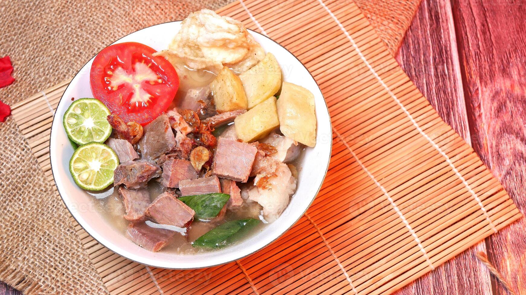 Delicious clear beef soup garnished with fresh potatoes, tomatoes, lime and fried onions. Served in a traditional style on a bamboo coaster. Space for text available photo