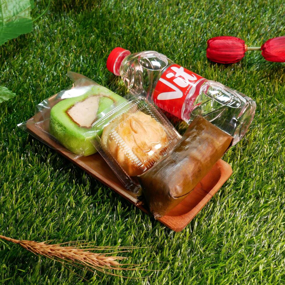 Jakarta, Indonesia. December 24, 2024. Snack box package traditional Indonesian cakes, cream puffs, roll cakes, and lemper delicious and a bottle of mineral water, with a natural decorative touch photo