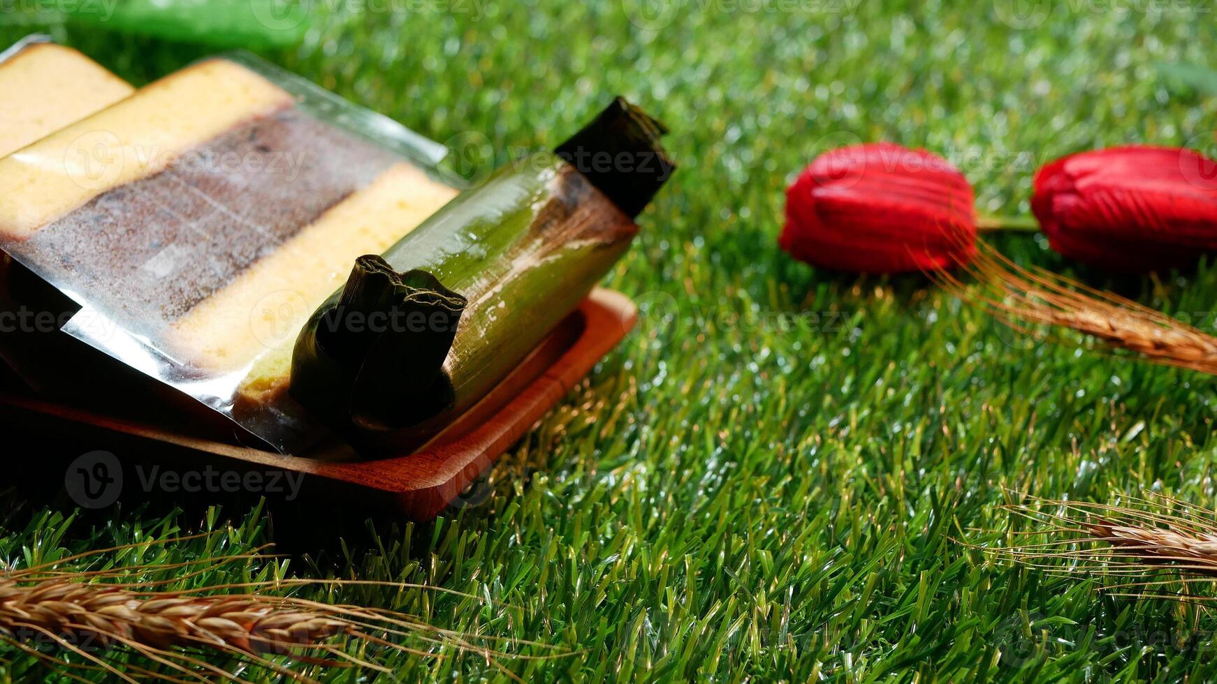 Selective focus on sweet and delicious layer cakes and Lemper, which are traditional Indonesian cakes, decorated with wheat stalks, red flowers and synthetic grass bases. photo