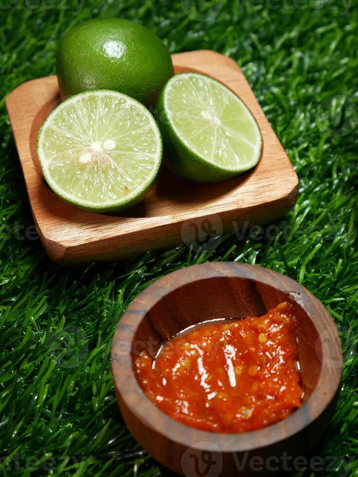 Closeup Traditional Indonesian food, sambal terasi and fresh lime served in a wooden bowl with a green synthetic grass base. photo