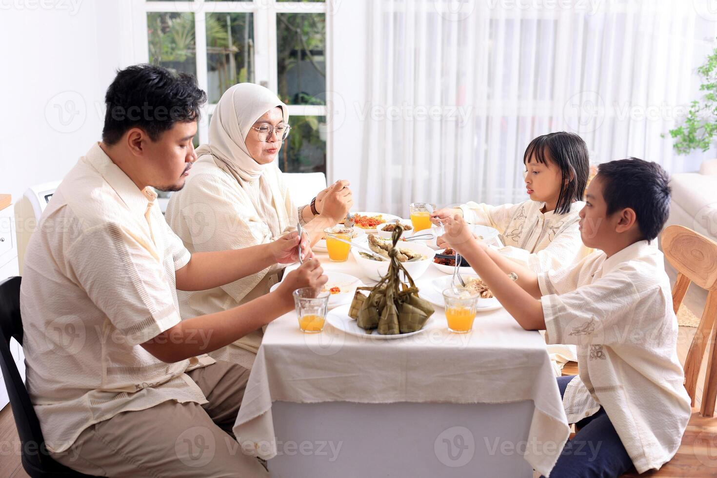 Young Asian Muslim Family , Father, Mother, and Two Kids Eat Ketupat Lebaran Together, Celebrate Idul Fitri photo