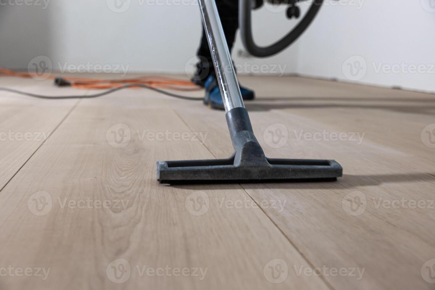 Light colored wooden floor with visible grain patterns being polished. An orange power cord and a person in blue shoe covers are partially visible. photo