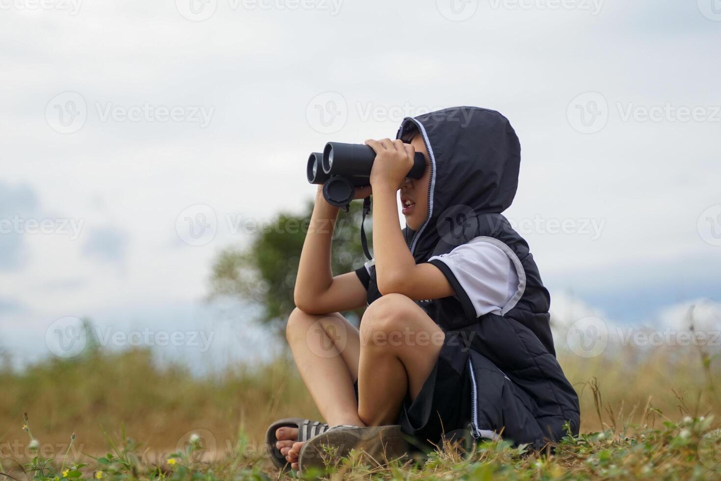 a boy uses binoculars to explore nature in the field. the concept of learning outside the classroom nature study, exploration. photo