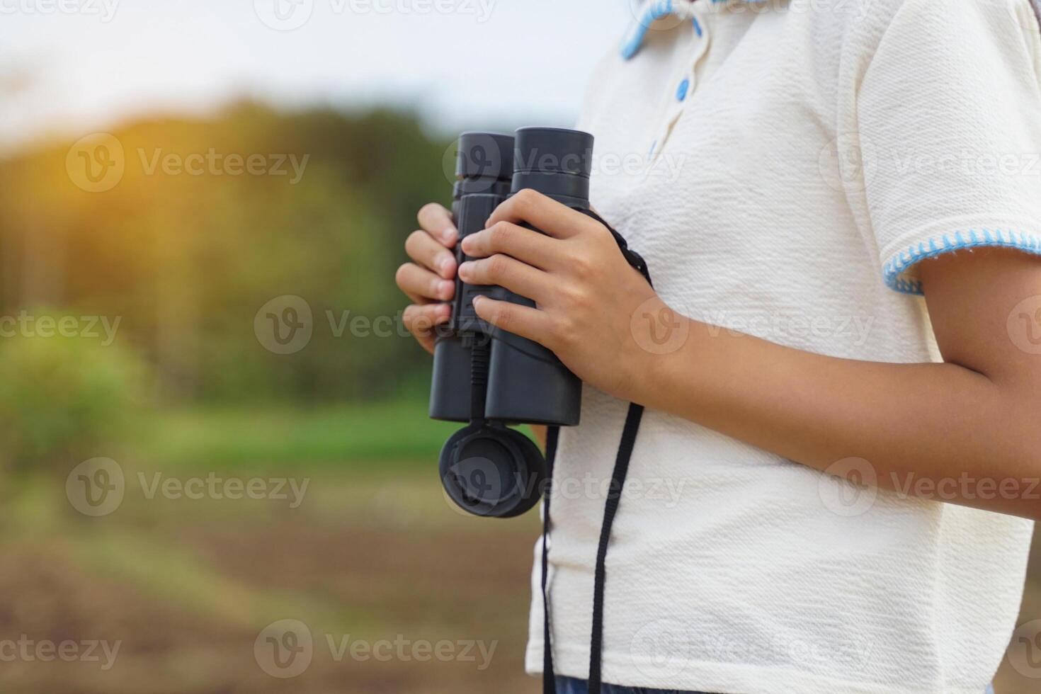 thai girl uses binoculars to explore nature in the field. the concept of learning outside the classroom nature study, exploration. photo