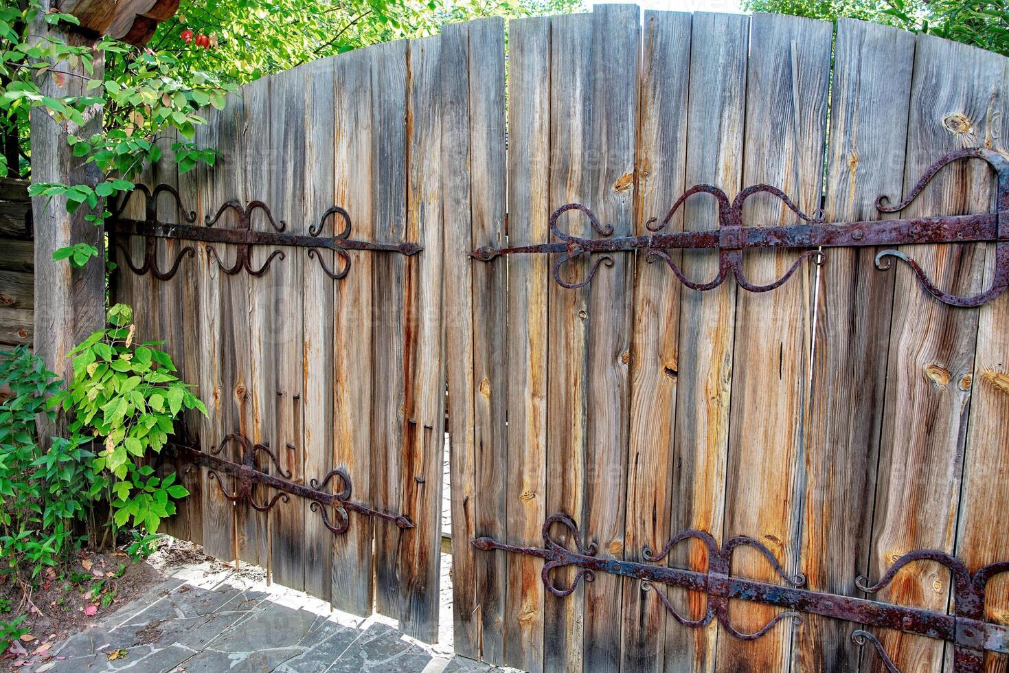 Rustic wooden gate adorned with iron hardware in a lush garden reveals a hidden sanctuary photo