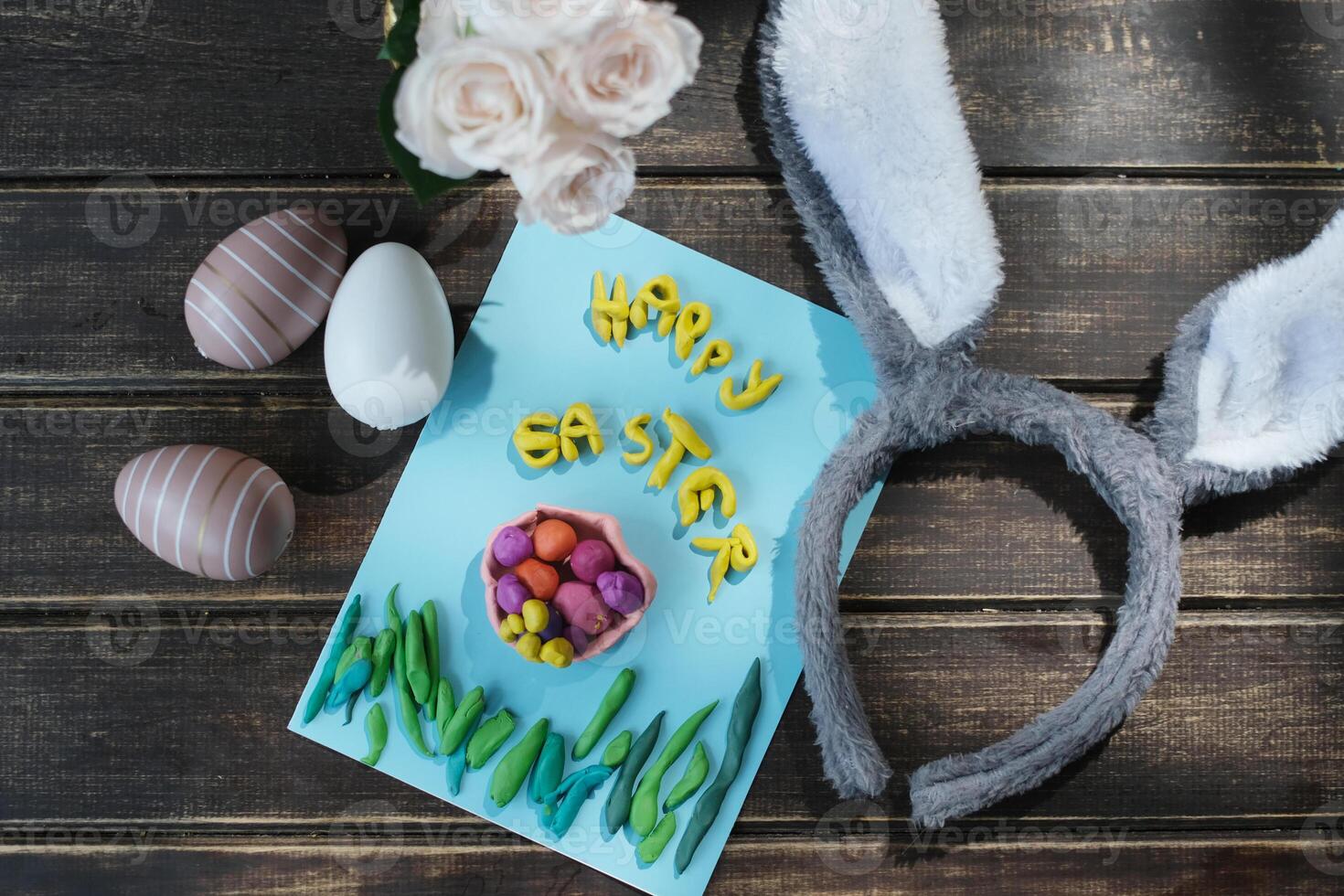 Happy easter concept. DIY childish greeting card, coloured easter eggs and bunny ears on wooden table. Top view. photo