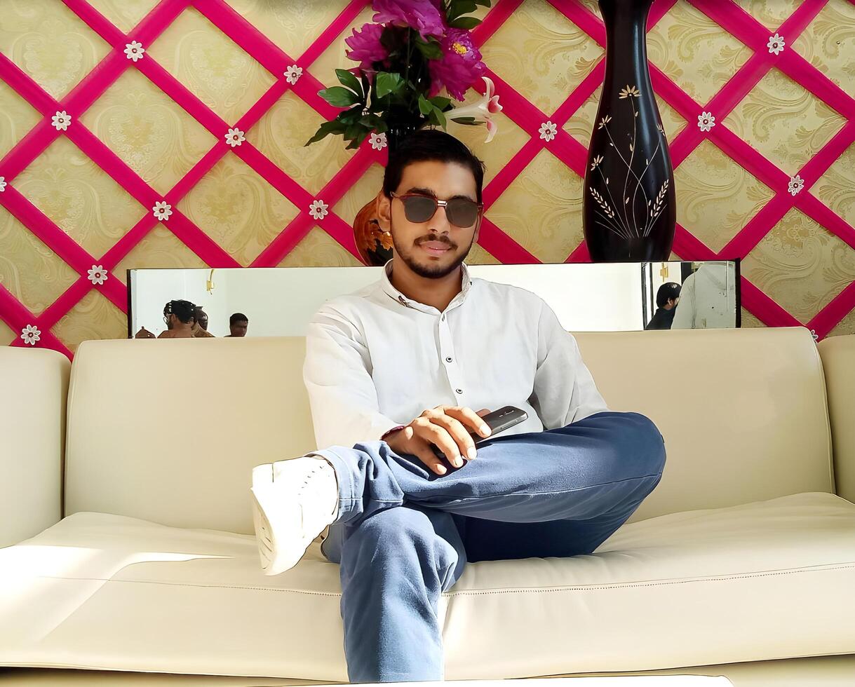 Young man sitting on a sofa, holding a mobile phone in his hand and looking directly at the camera with a casual expression photo