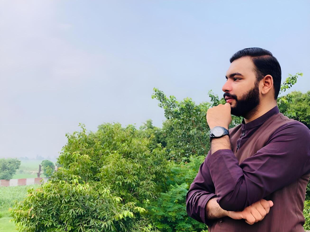 Handsome bearded Indian man in casual clothes standing outdoors, looking thoughtfully away from the camera photo