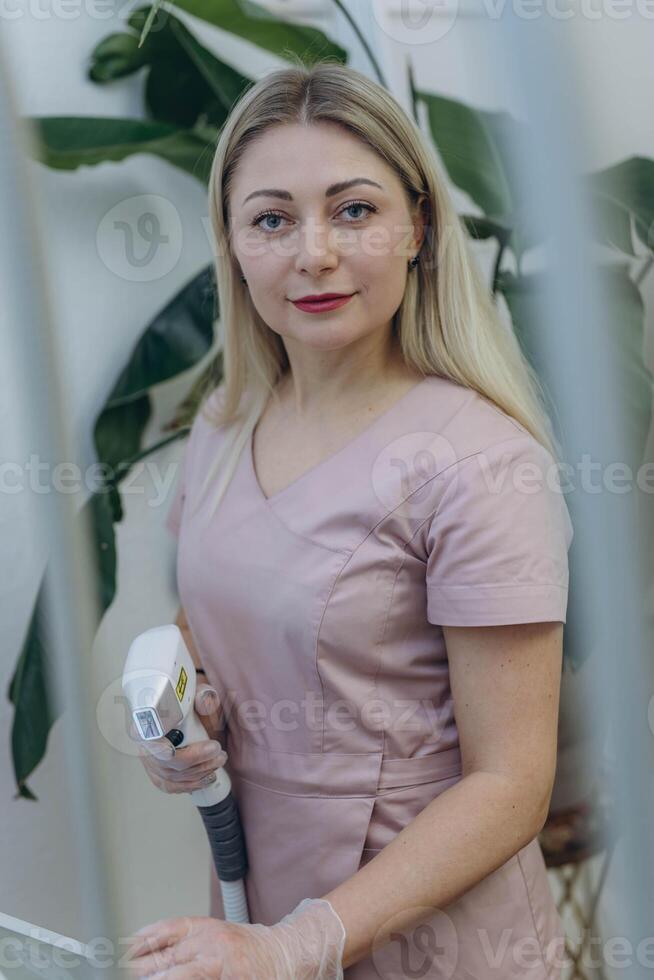 Smiling young woman laser hair removal expert holding a laser device in the cosmetology section photo