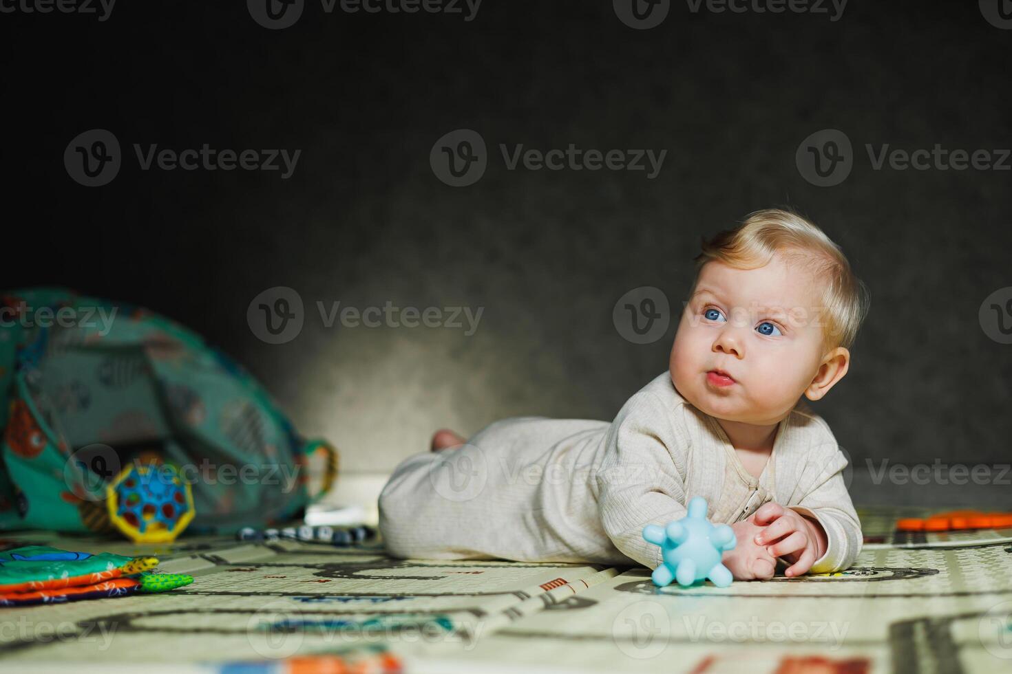 7-month-old baby is lying on a rug and playing. The child holds his head. A baby learns to crawl on the floor. A child in a beige romper. photo