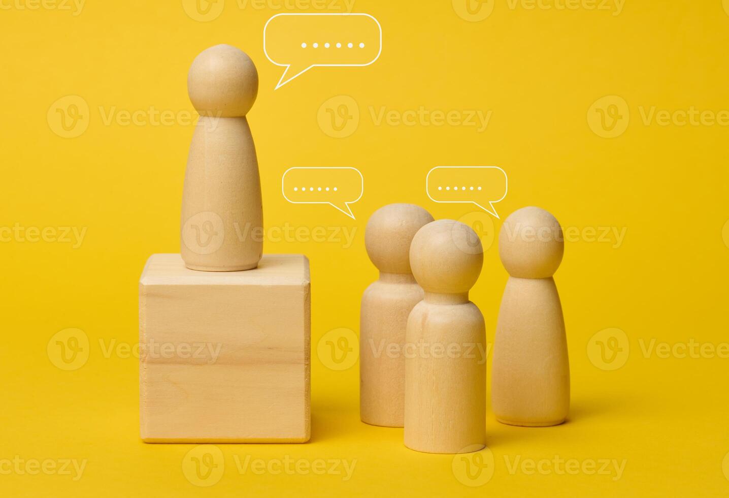 Wooden figures on a yellow background symbolize communication and leadership, one figure stands on a pedestal photo