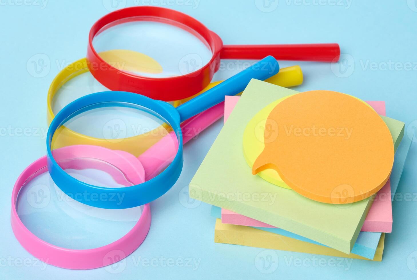 Multicolored plastic magnifying glasses on a blue background and paper notes photo