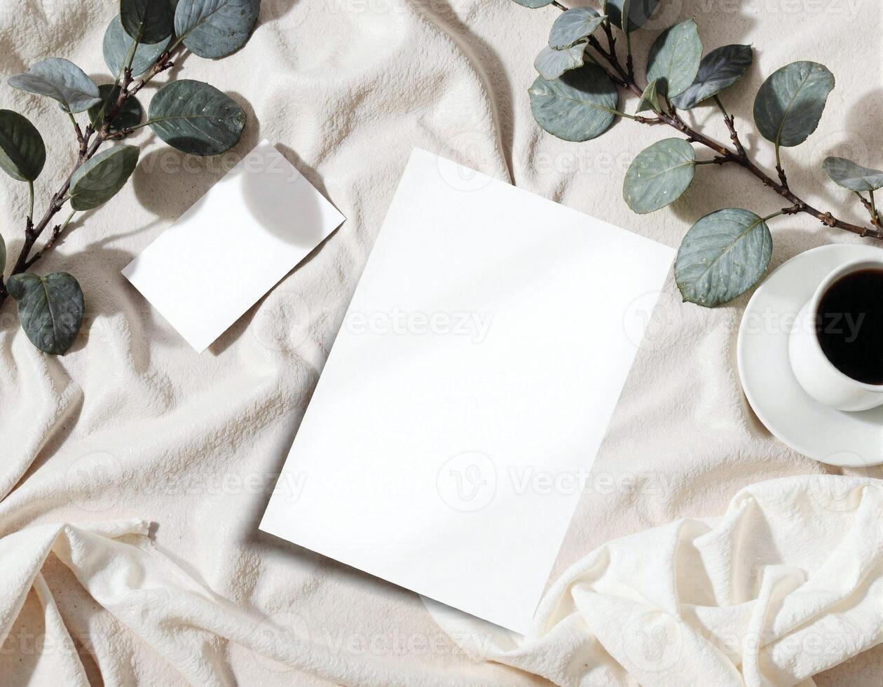 Blank paper, coffee cup, and eucalyptus leaves on a white linen photo