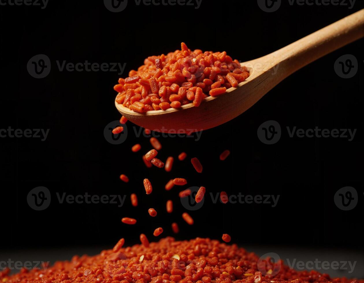 Falling red chili flakes from a wooden spoon on a black background. photo
