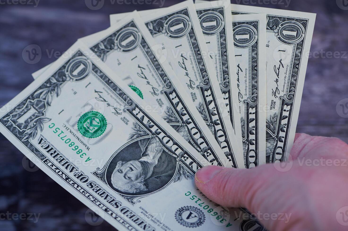 Hand holding multiple one dollar bills in a casual setting with dark background photo