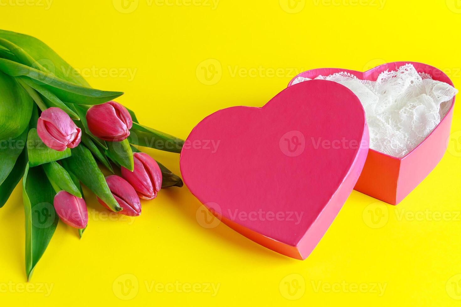 Tulips and pink heart shape box on yellow background. photo