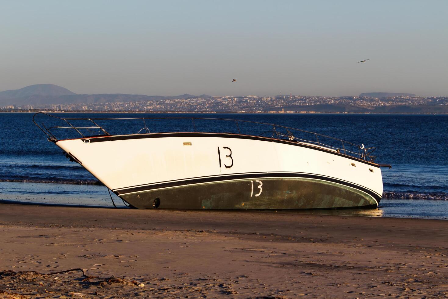 San Diego, CA, 2024 - Demasted Sailboat Aground On Sand Beach With Ocean photo